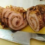 Skivad köttfärsrulle med kryddor på en skärbräda med en kniv bredvid.