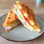 En sandwich med skinka, tomat och sallad på en tallrik, skuren i halvor.