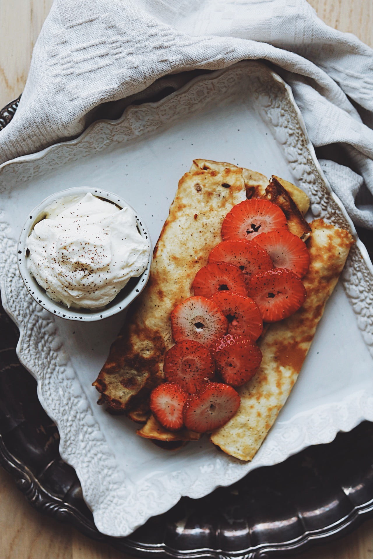 Pannkakor på en tallrik med jordgubbar och grädde i en skål bredvid.