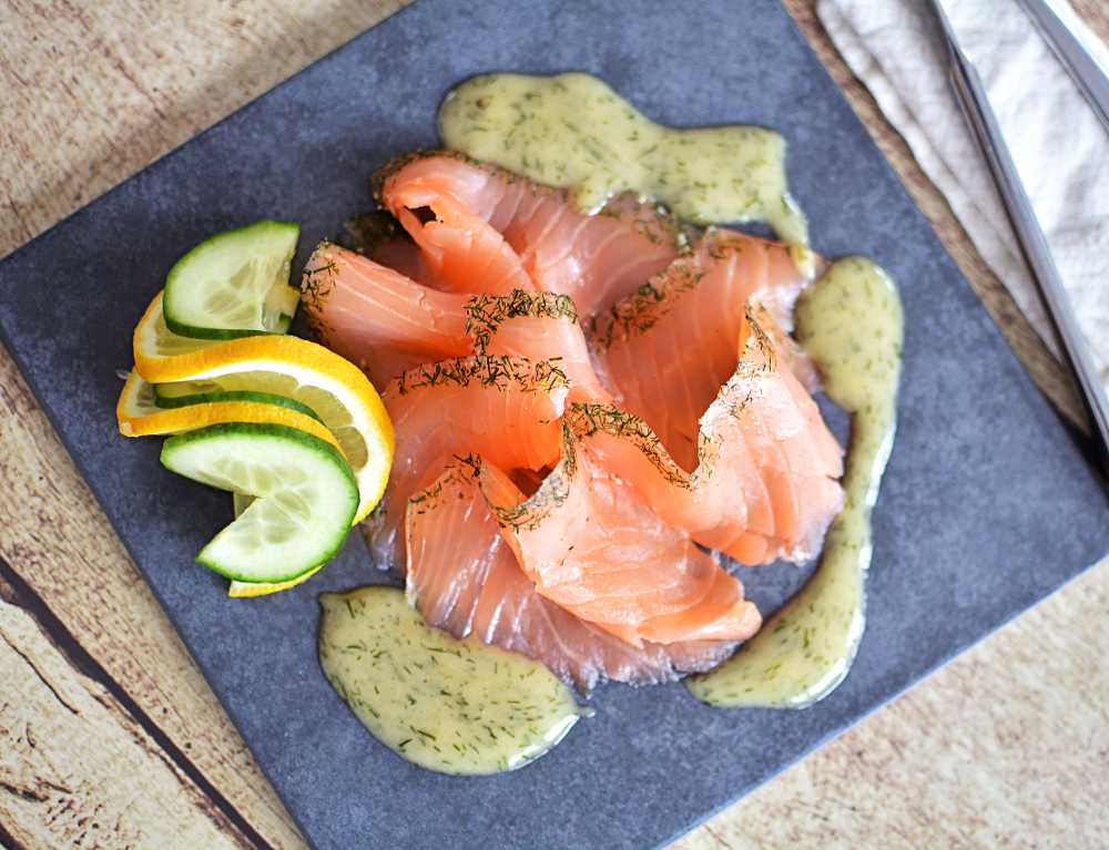 Gravad lax 6 En tallrik med skivad gravlax sedd uppifrån med hovmästarsås runt.