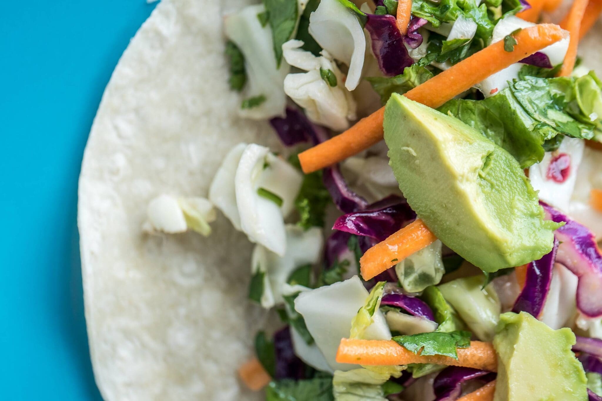 Tortilla fylld med grönsaker som morötter, kål och avokado på en blå tallrik. Tortilla fylld med grönsaker som morötter, kål och avokado på en blå tallrik.