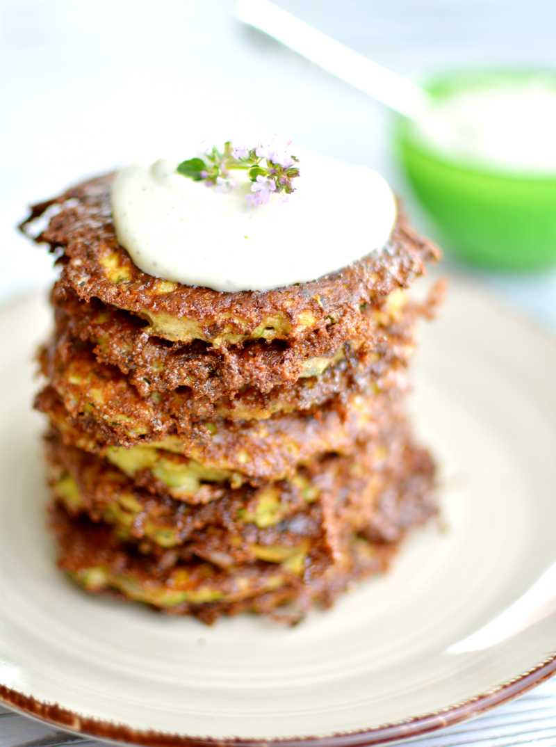 En hög av zucchinifritters med en klick gräddfil och örter på toppen. En hög av zucchinifritters med en klick gräddfil och örter på toppen.